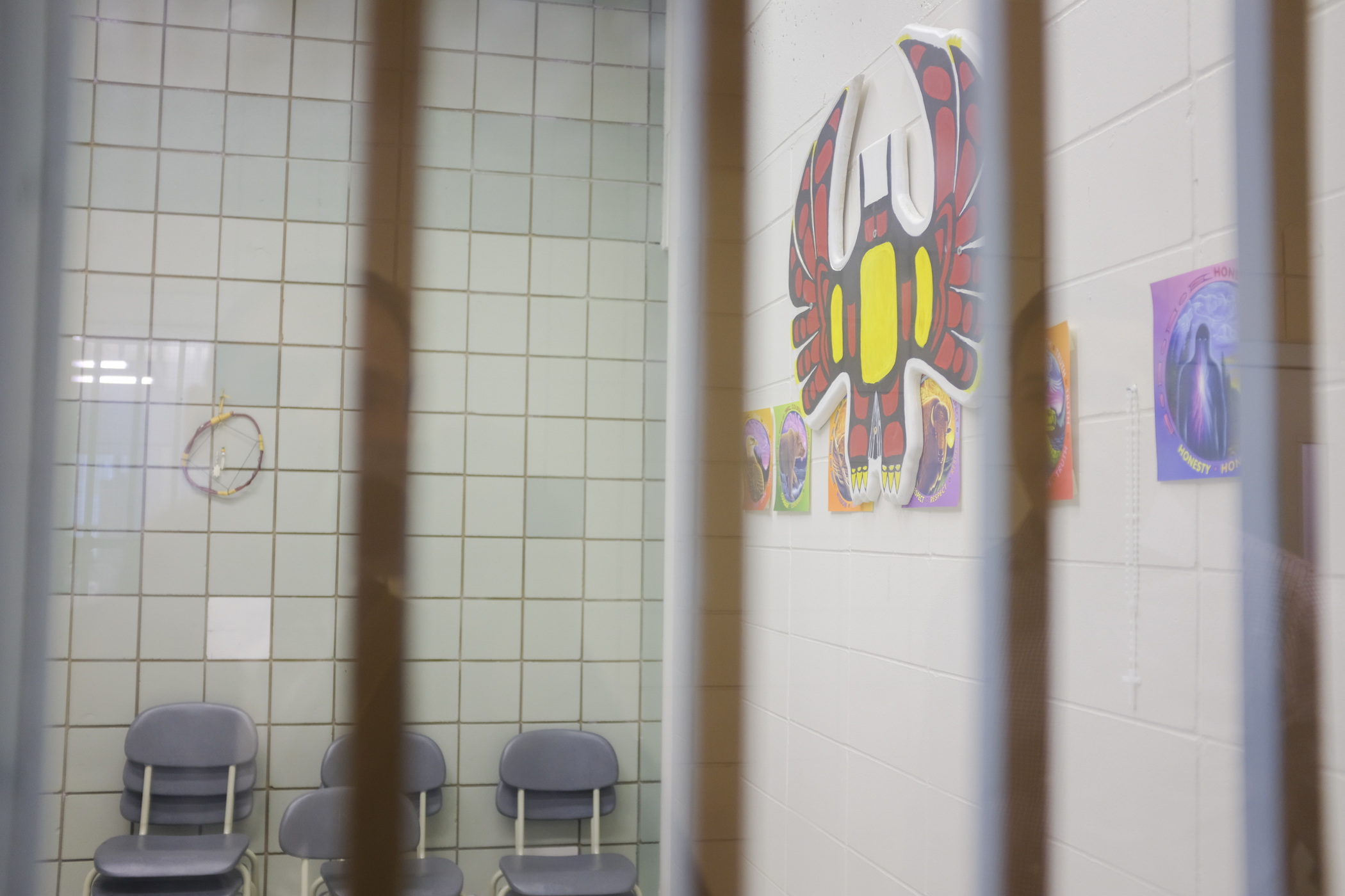 Photo of a programs space at Donnacona Institution looking through a barred window. An Indigenous mural can be seen on the wall of the room.